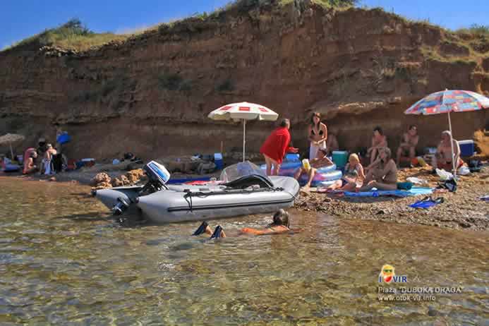 Gumeni čamac sa motorom usidren na pješčanoj plaži sa turistima