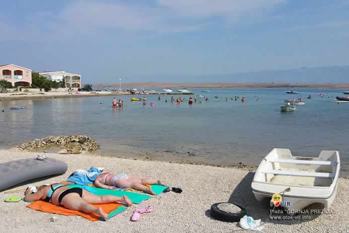 Bijeli čamac na šljunčanoj plaži pored dviju osoba koje se sunčaju