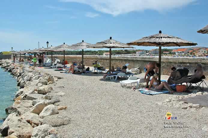 Drveni suncobrani i plastične ležalje za innajmljivanje na šljunčanoj plaži Jadro na Viru
