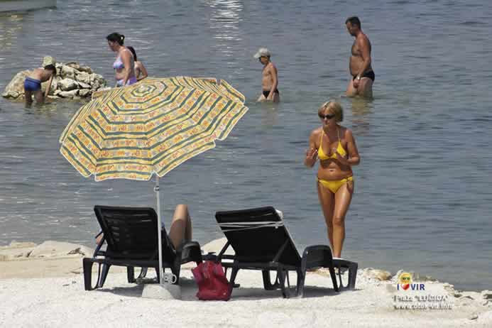 Ležaljke i suncobran pored mora sa kupačima
