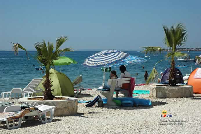 Turisti odmaraju na bijeloj klupi pod suncobranima pored palma i rekvizita na plaži