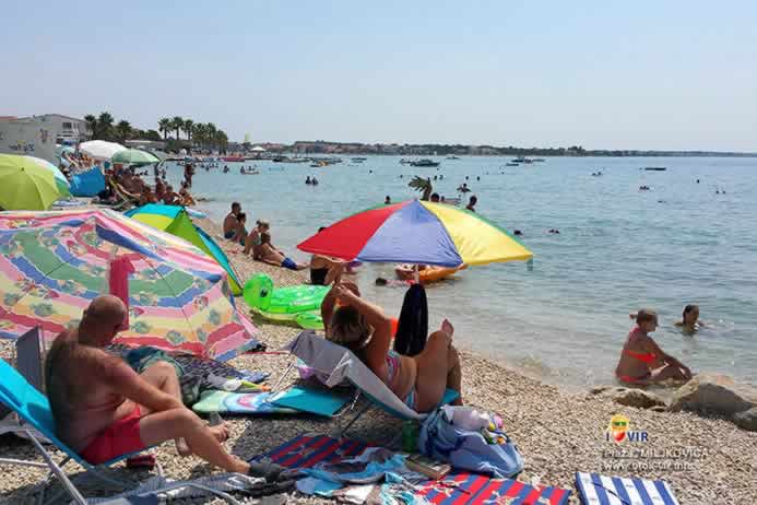 Turisti uživaju pod suncobranima na plaži dok se djeca kupaju u moru