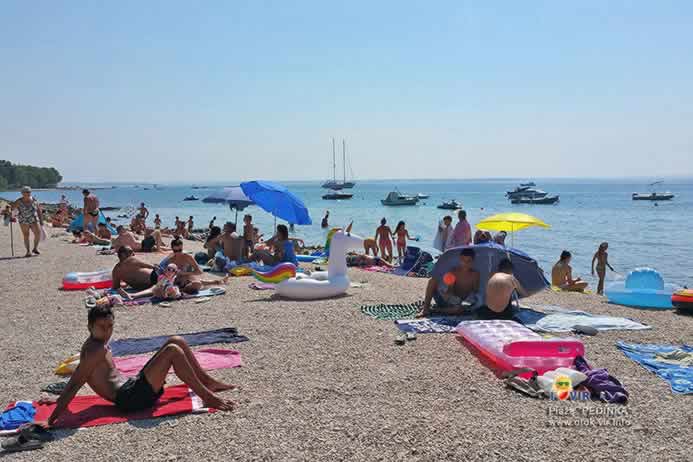 Kameno šljunčana plaža s turisitma i usidrenim čamcima