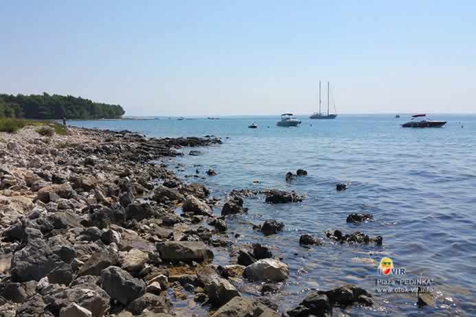 Kameno šljunčani dio neuređene plaže s brodovima na pućini