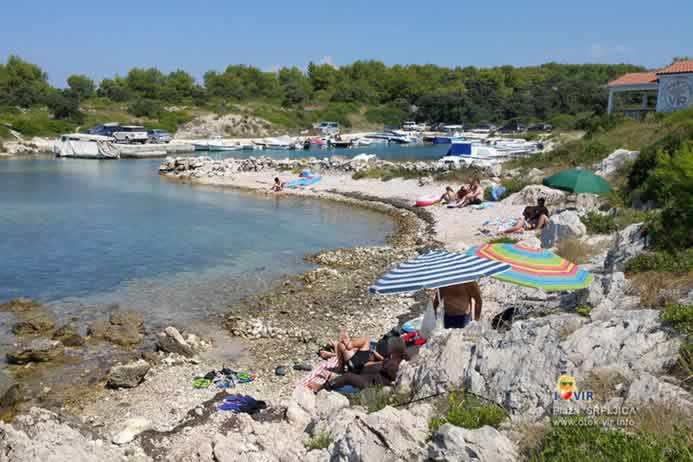 Sunčanje turista pored mora na kamenoj plaži ispred lučice za brodove